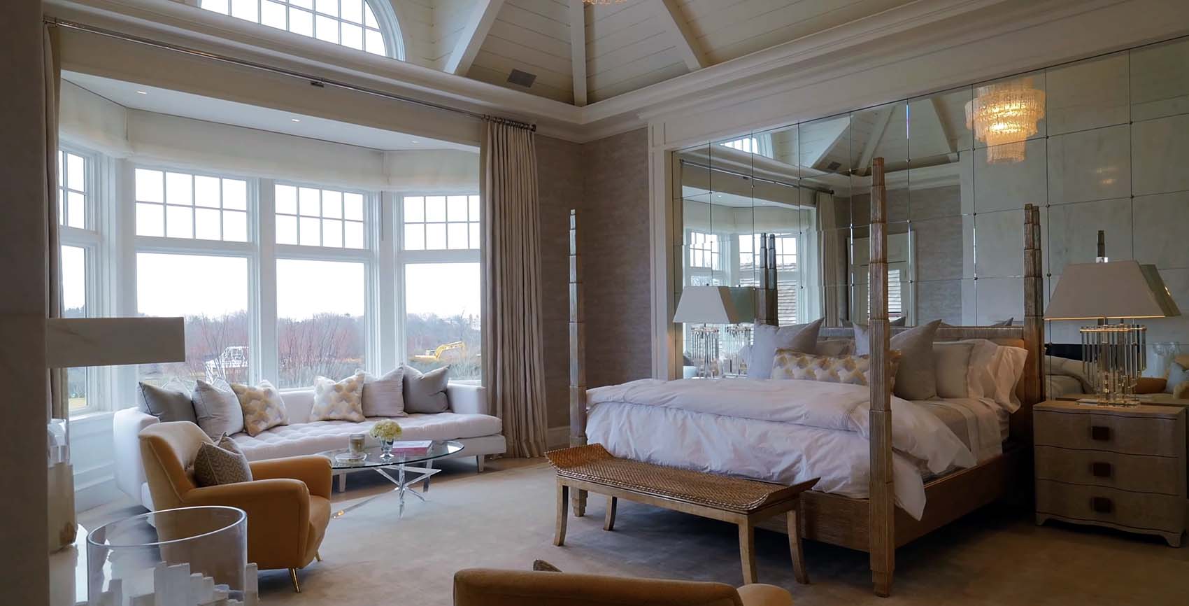 master bedroom with tan colors caulted wood ceilings huge windows mirror wall sitting area