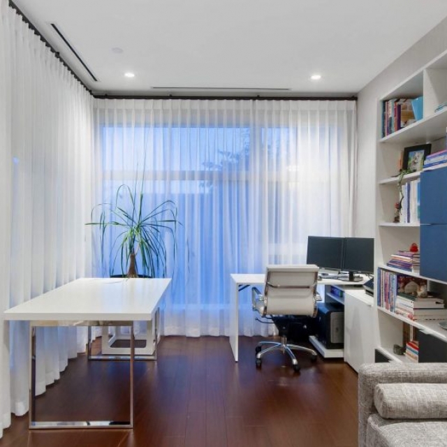 Modern home office, dark wood floors, white furniture, white and chrome desk, gray sofa glass walls.