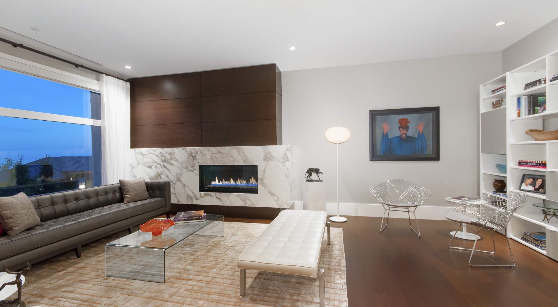 Modern gas fireplace with huge marble surround, medium dark wood floors with area rug, glass coffee table