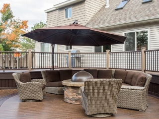 NJ Custom trex deck with curved design, stone fire pit, wicker furniture with brown cushions and umbrella, brown railings, multi level deck