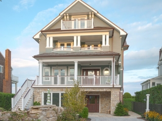 Gray vinyl siding color scheme with brown gutters and white trim. White square columns and railings with a wood hand rail. Brown stone veneer. Brown front door. Real stone landscaping.