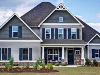 Two toned blue and gray siding colors with black front door. White trim with blue shutters. Brown stone veneer.