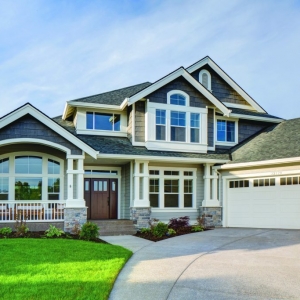 Two toned light and dark gray siding colors with white trim and columns with white railings. White garage doors. Dark brown stained front door. Light brown stone veneer.