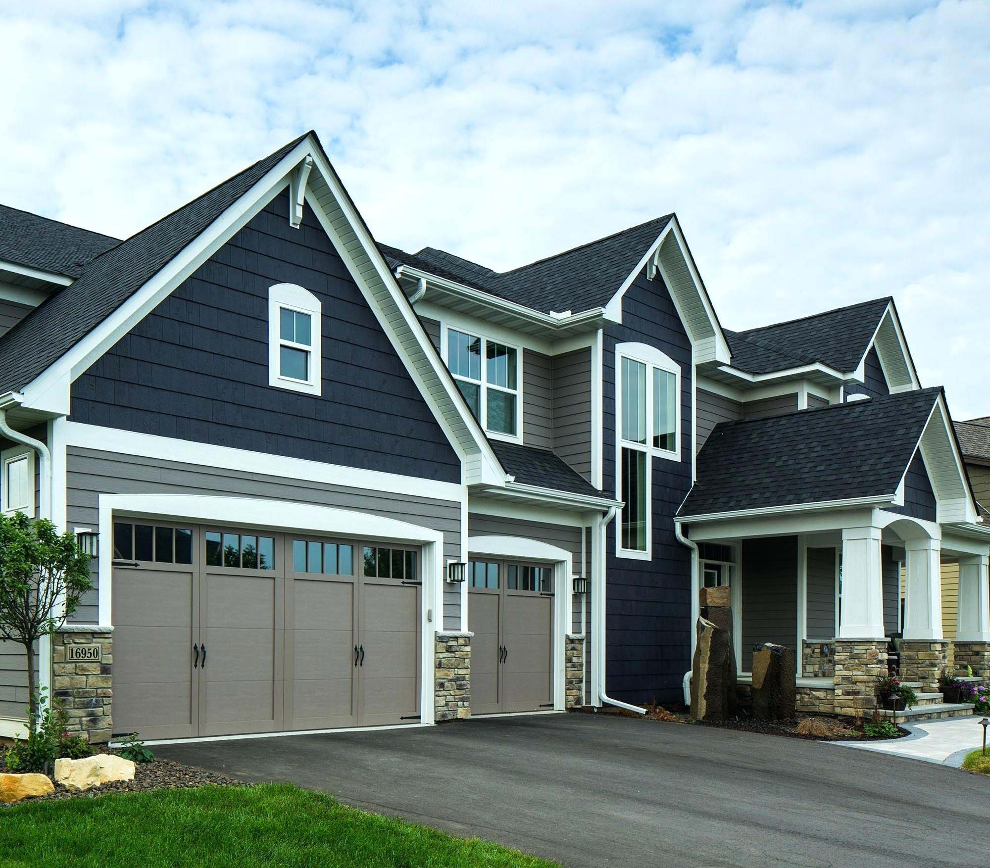 Two toned blueand gray siding color combination. Black roofing shingle. Taupe garage doors. Brown stone veneer. White trim and columns.