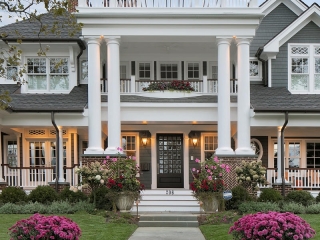 gray house siding color with white trim and huge white columns, black front door, brick veneer, brown gutters. White rails with brown wood hand rail. red brick chimney.