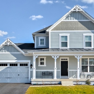Blue, gray and white siding color scheme. White trim and columns. Black metal accent roof. Black shingled roof. Vertical siding accents. White garage door with black front door.