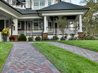 Dark gray siding colors with thick white trim and columns. White railings with a wood hand rail. Brick paver walkway. Dark shingle roofing with brown gutters. Brick column bases.