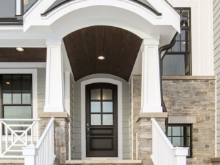 Light gray siding color with tons of white trim and white wall paneling. Dark brown wood porch soffit with recessed lighting. Tapered porch columns with white rails. Stone veneer. Black gutters. Black framed windows.