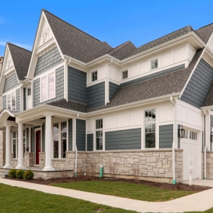 Blue vinyl siding with white wall paneling and trim. Round porch columns. Light tan stone veneer. Red fron door. Gray shingle roofing. White garage doors.
