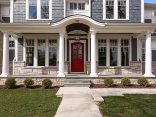 blue vinyl siding color with white trim, wall paneling and round columns. Red front door. Dark brown wood porch soffit. Light brown stone veneer. Concrete walkways.
