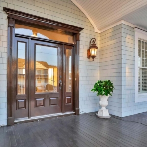 Front porch with light gray cedar shake siding, dark brown stained wood front door, white trim and soffit with recessed lighting. Dark brown stained wood front porch.