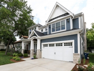 Blue vinyl siding colors. Light tan stone veneer. White garage door. White trim and wall paneling with blakc metal accent roof. Black shingled roof. Tapered porch columns. Black porch railings.