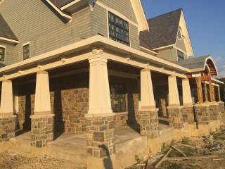Light gray cedar shake siding colors, white tri with tapered porch columns, light brown stone veneer, blue shingled roof, concrete front porch top.