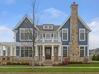 Blue siding colors with brown stone veneer. White trim with square coluns and arbor. Stone chimney. Black shingled roof.
