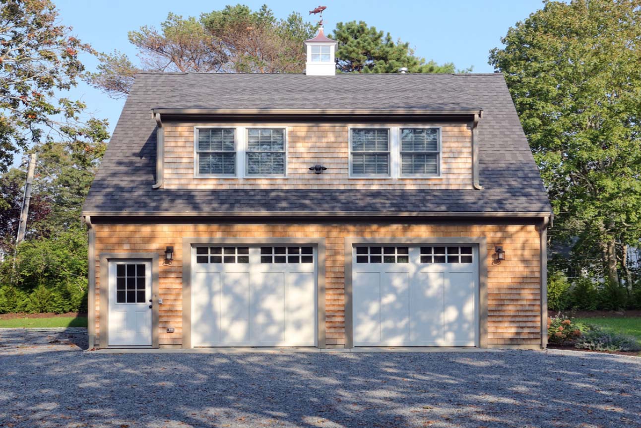 Two car garage design with second floor living space. White doors with gray trim. Real wood cedar shake siding.