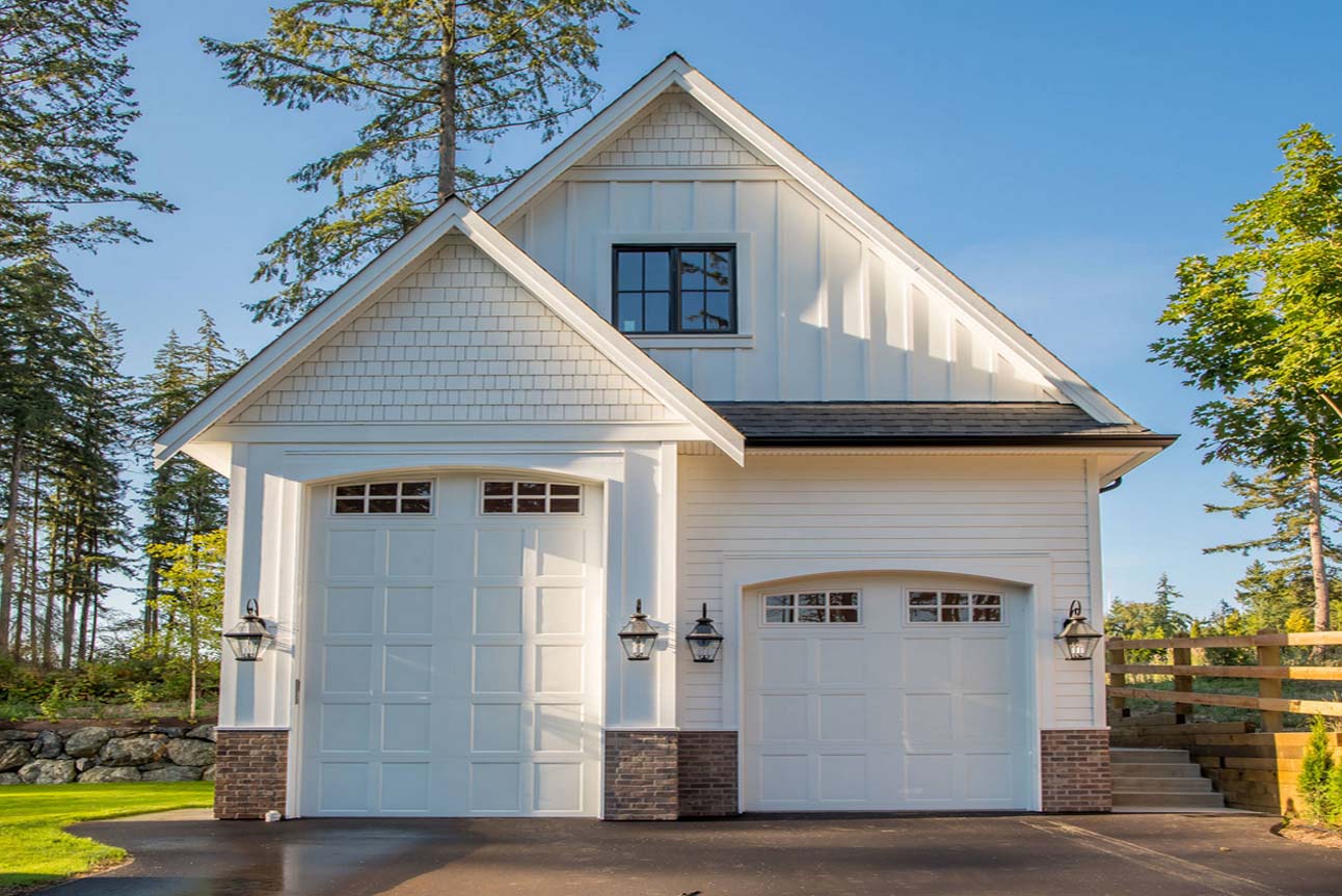 Two car oversized garage. One bay large enough for a bus. White siding and trim with white doors. Red brick veneer. Black framed windows with vertical siding accents.