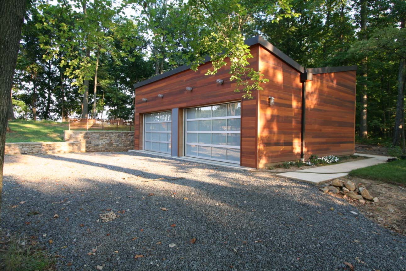 Modern 2 car detached garage design. Ipe wood siding. Black metal roofing and trim. Metal and glass garage doors. Gravel driveway.