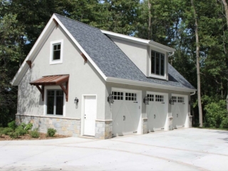 3 Car detached garage design with gray stucco veneer siding and real stone base veneer. White garage doors with white trim. 2nd Floor living space. Brown metal accent roof.