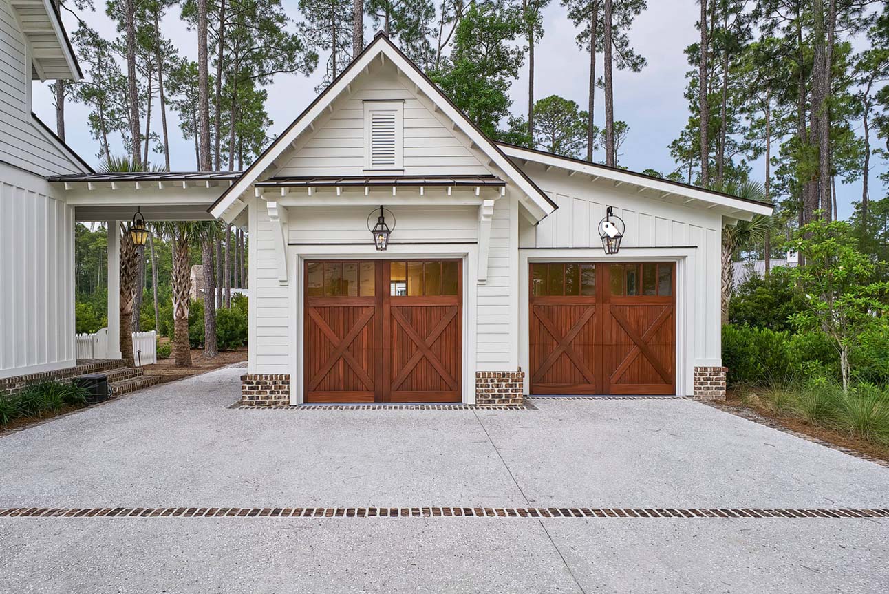 2 Car detached garage design with breezeway. Horizontal white lap siding. White trim. Stained brown wood doors. Architectural details. Red brick base veneer. Metal accent roof. Fancy garage design.