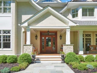 Neutral house siding colors. Light tan with a brown stained wood front door. Light gray stone veneer. White trim. White columns. Blue stone walkway.