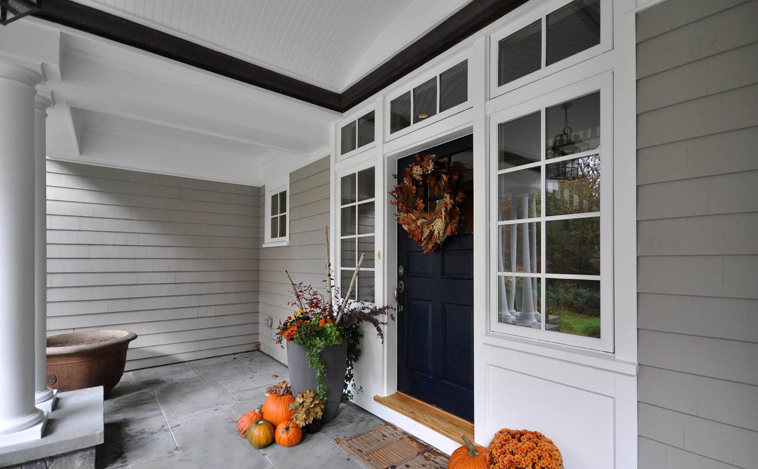 Gray house siding color scheme with dark blue front door. White trim and wall paneling. Blue stone front porch top. White columns.