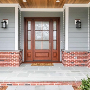 wood front door with glass and transoms gray siding with red brick house and blue stone patio