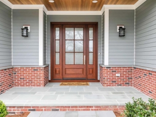 wood front door with glass and transoms gray siding with red brick house and blue stone patio