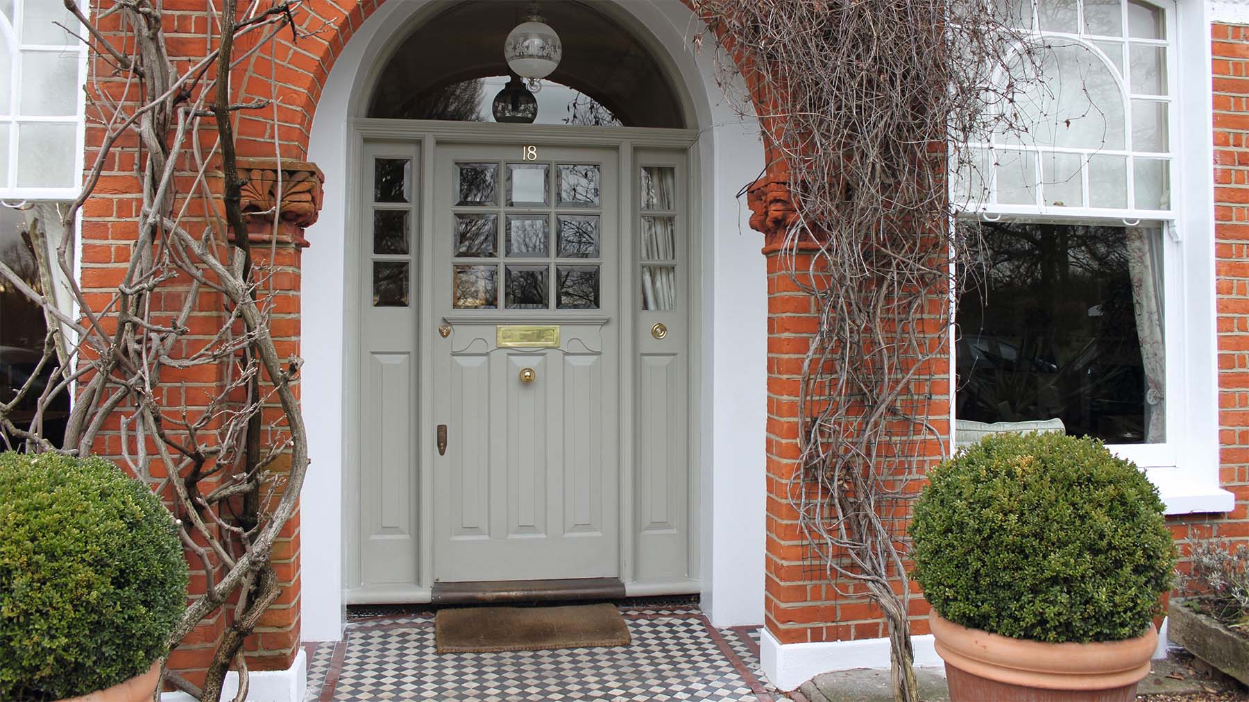 Light gray front door with transoms white trim and red brick house green porch plants vines