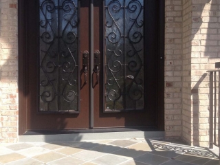 Dark brown front door with black iron scroll work with red brick house