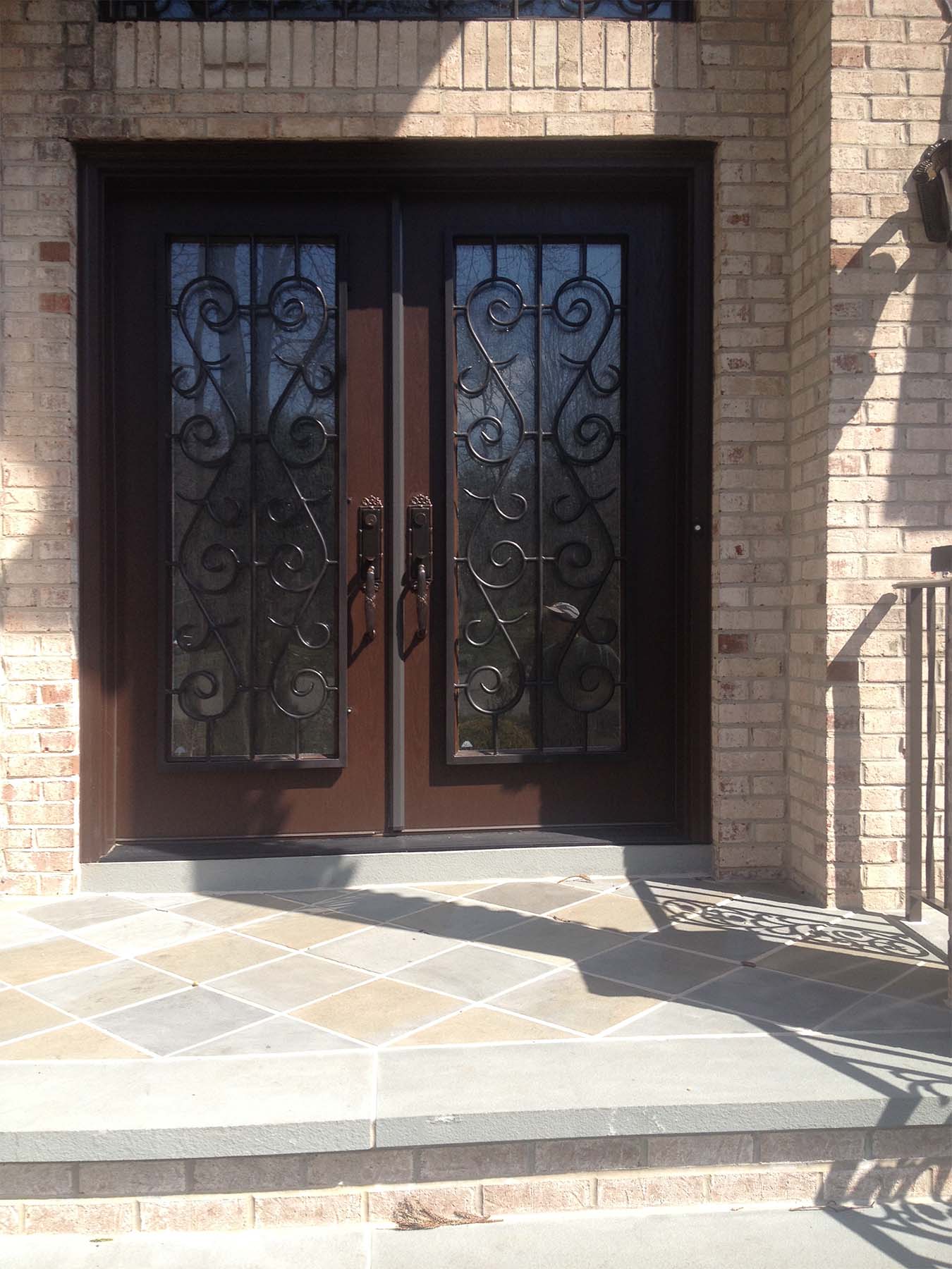 Dark brown front door with black iron scroll work with red brick house
