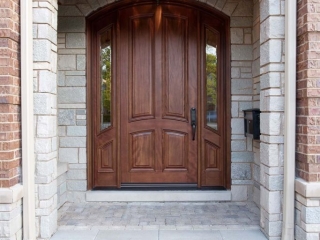 Natural wood curved front door with stone on a red brick house