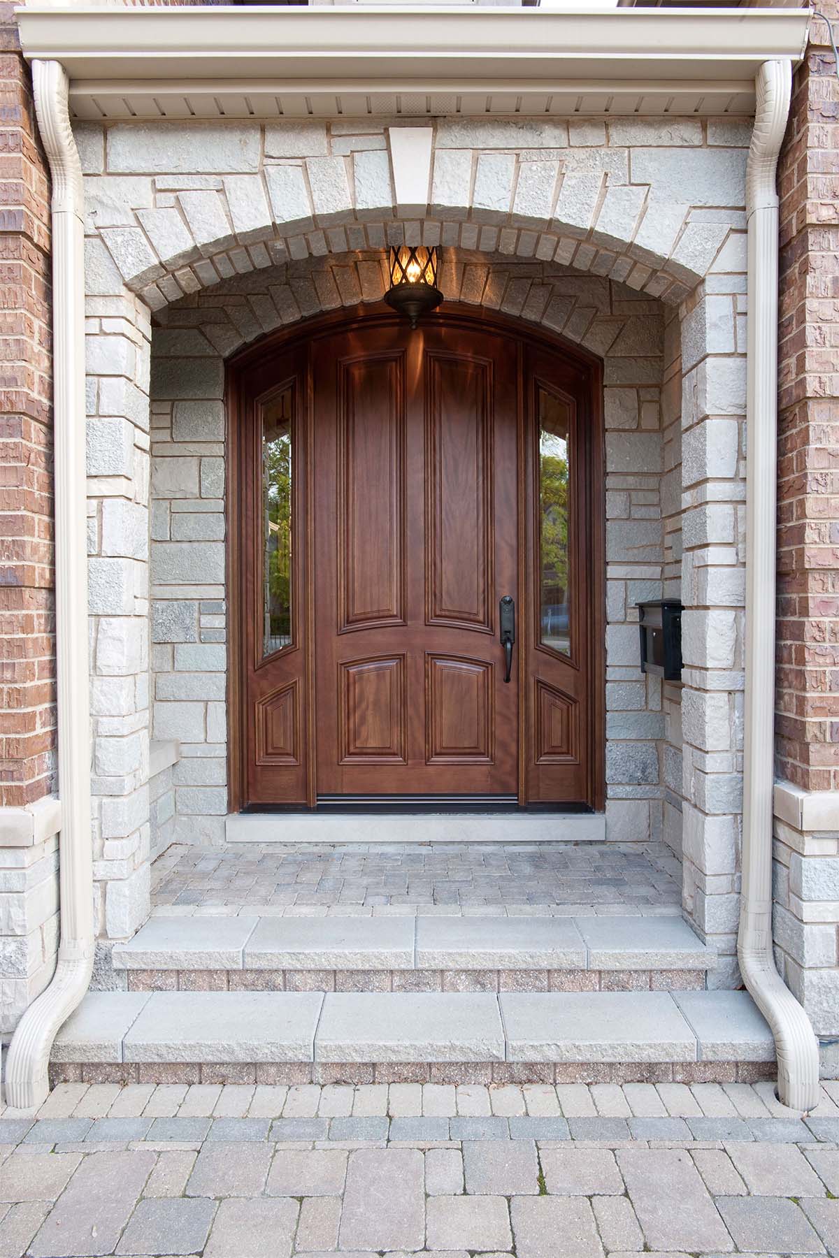 Natural wood curved front door with stone on a red brick house