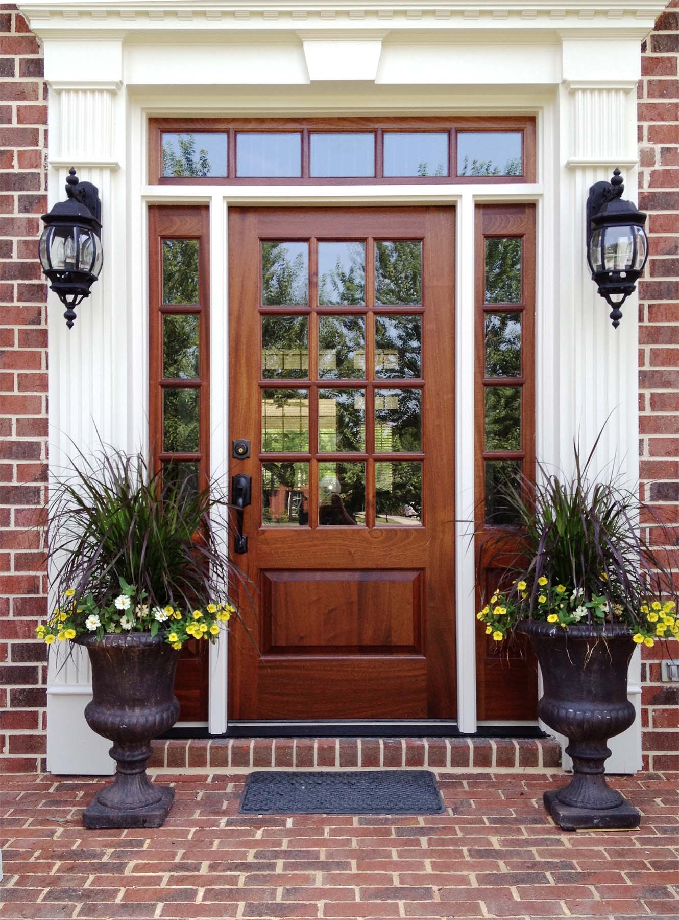 beautiful Natural wood front door with glass transoms white trim red brick house colorful porch plants