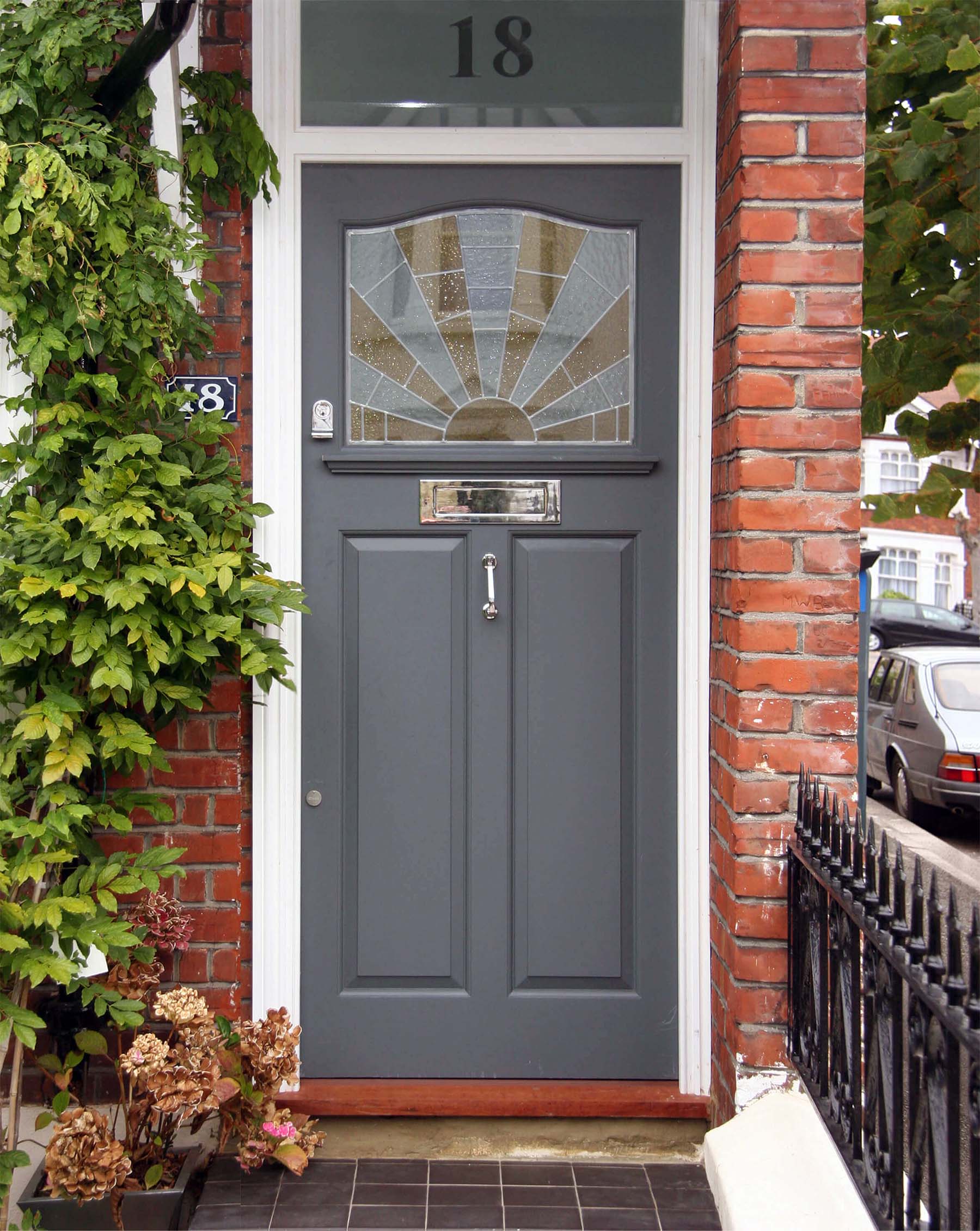 gray front door with red brick house and stained glass with silver mail slot