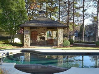 Beautiful small pool house design with real stone veneer siding. Real wood doors and an outdoor fireplace. Concrete patio surround. In ground pool.