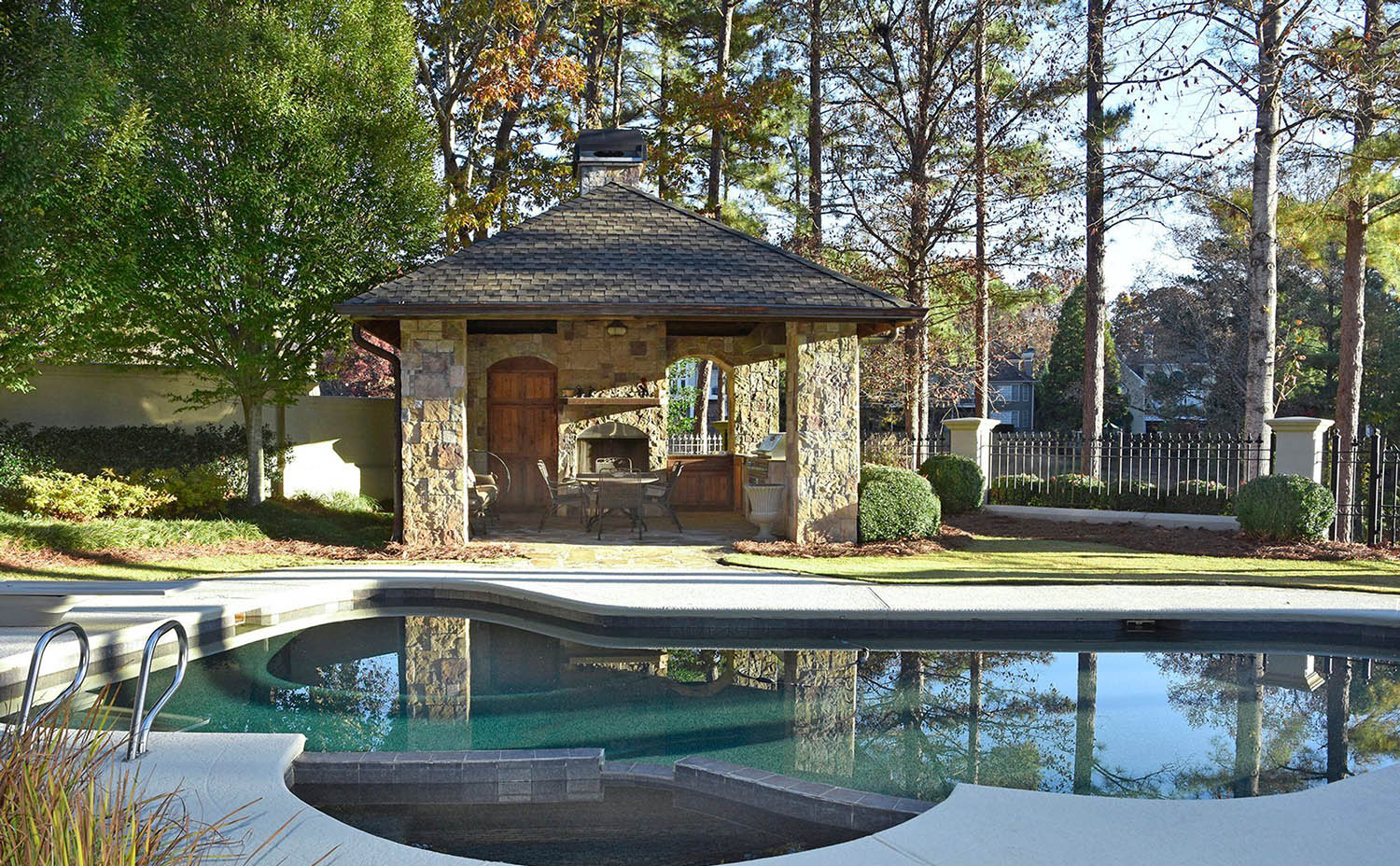 Beautiful small pool house design with real stone veneer siding. Real wood doors and an outdoor fireplace. Concrete patio surround. In ground pool.