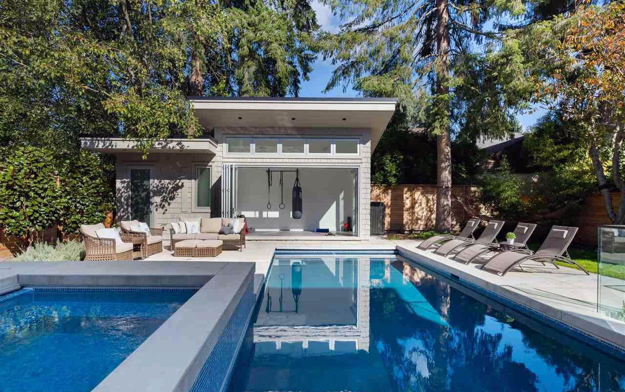 Modern pool house design. Rectangle in ground pool with hot tub. Pool side furniture. Wicker chairs with white cushions. Workout home gym. Folding glass patio doors. Flat roof.