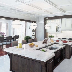 Luxury kitchen with marble countertops and dark brown island and white cabinets white coffered ceiling.