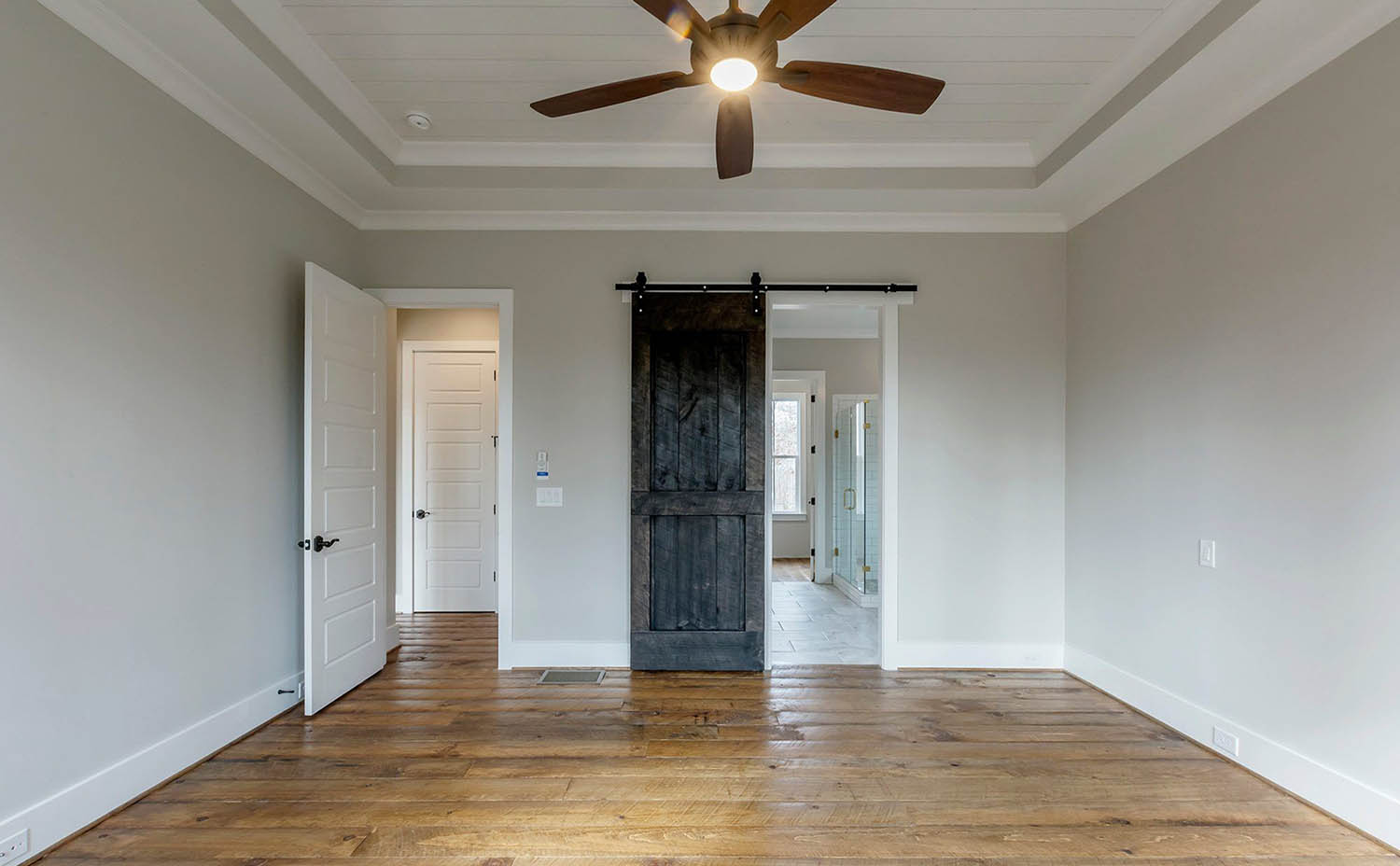 French style interior barn doors with black handles and mounting hardware. Beautiful white painted finish perfectly matches the walls and trim. medium stained wood floors.
