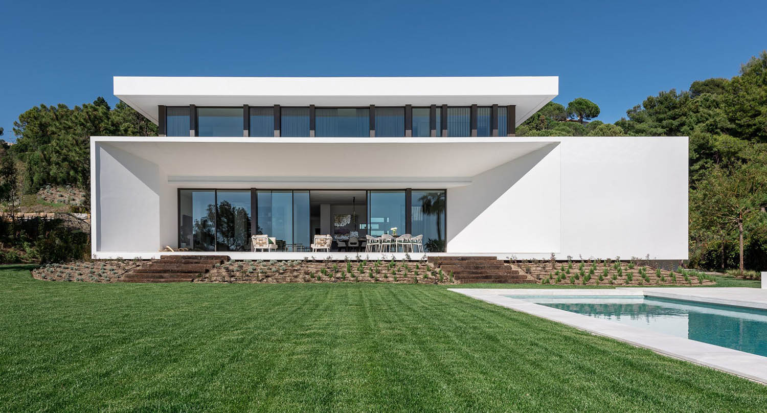 Beautiful contemporary flat roof house design with white stucco siding. Floor to ceiling glass walls. Black frames. In ground pool with cement patios.