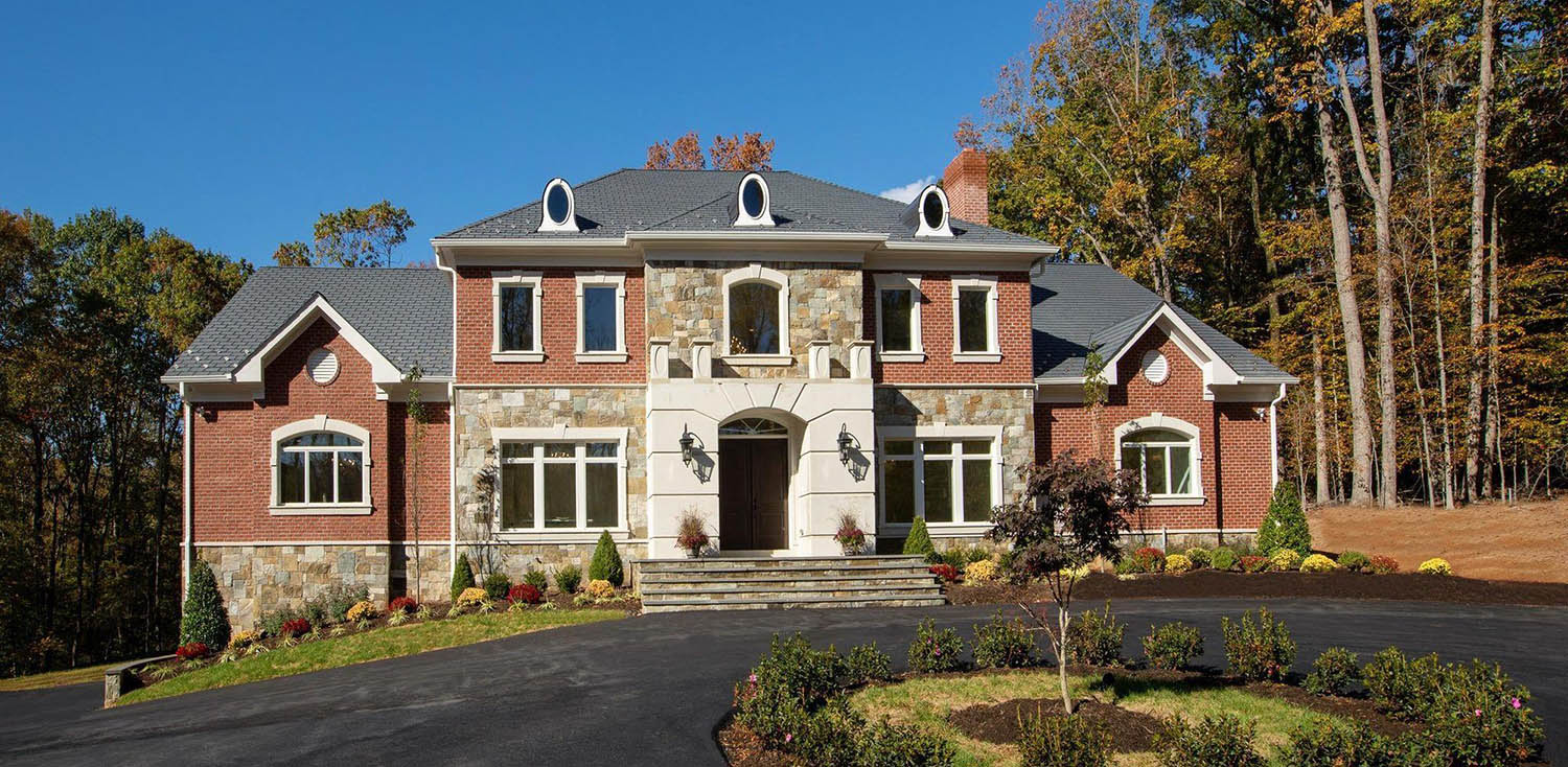 Red brickhome with stone and stucco veneer. Dormers on a black shingled roof. Stone steps.