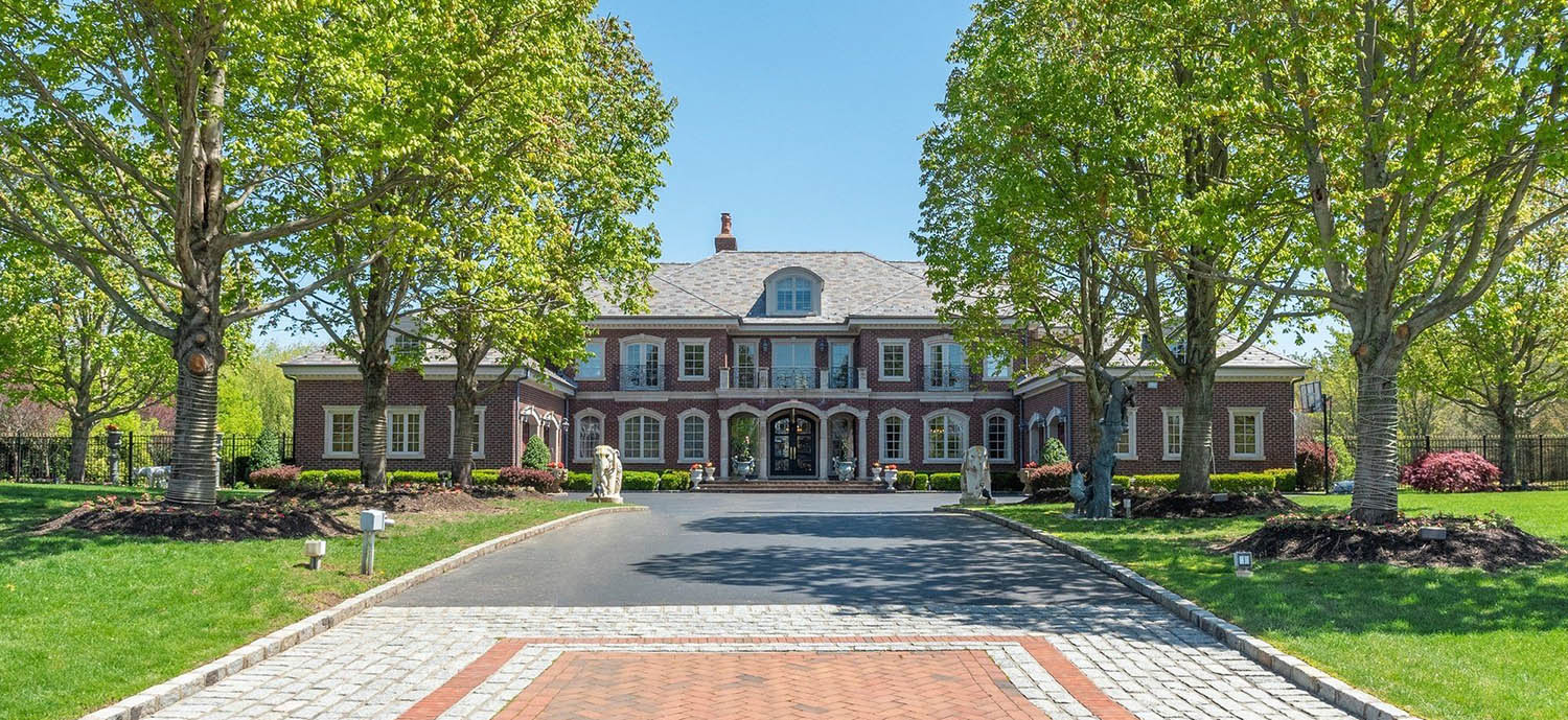 Huge red brick estate home, brick walls with stone trim and columns, arched dormer, gray roof shingles, black arched front french door.