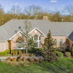 large red brick ranch style home with a dark gray roof shingle. Black metal accent roofing. Beautiful green landscaping.