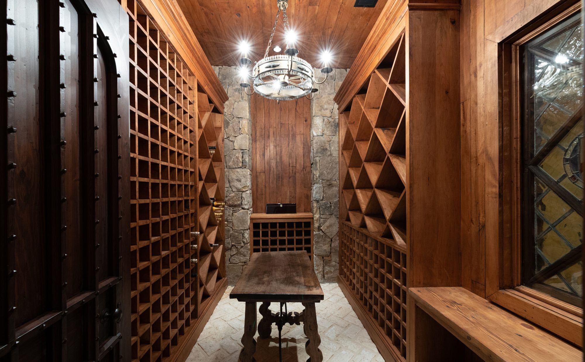 Beautiful wine room featuring wood and stone with a paver floor. Custom made wood door. Wood ceiling.