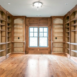 Library / office with all wood wall paneling and built in shelving. Matching hardwood floors. White ceiling.