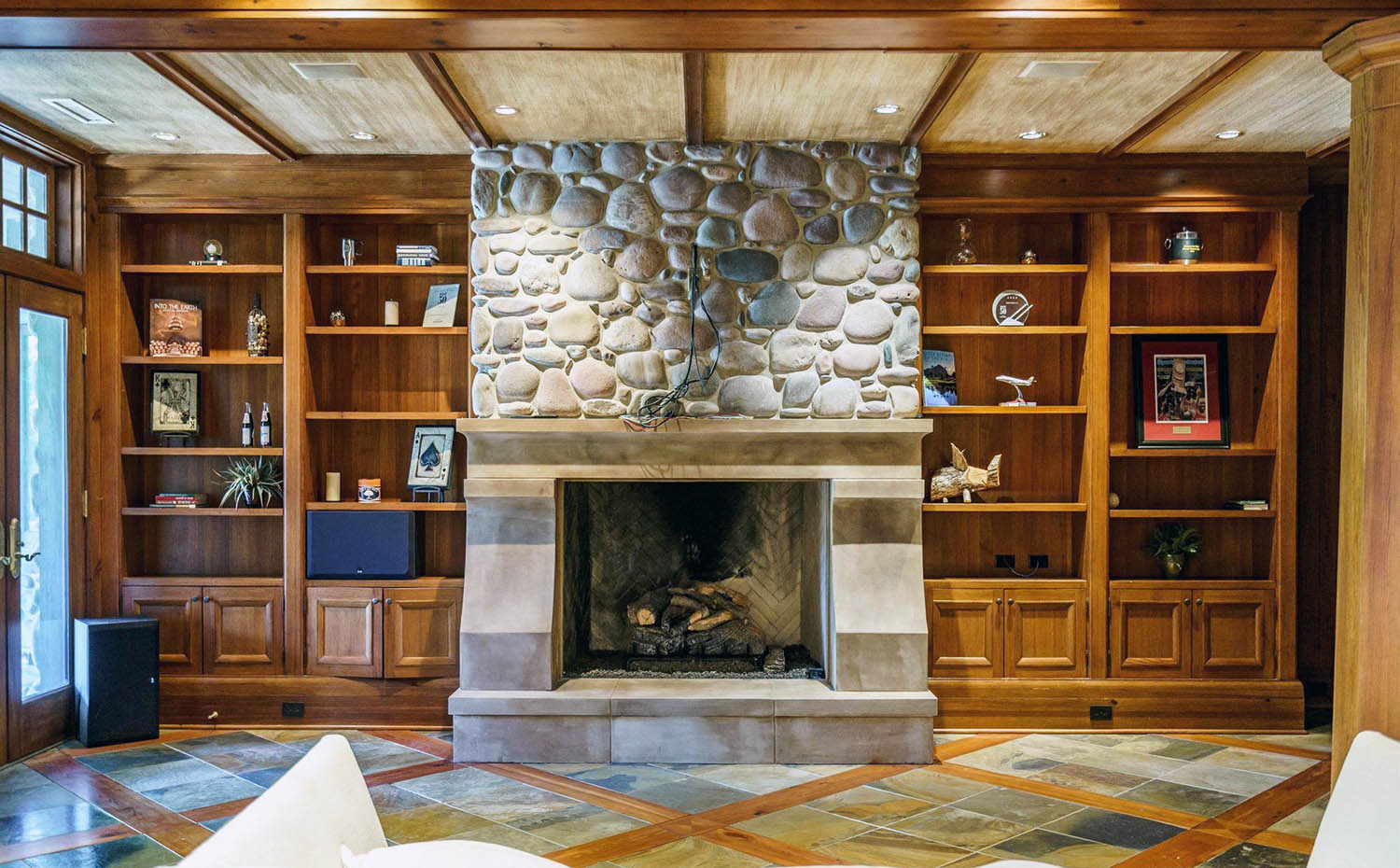 Room with all wood walls and ceiling. Real stone fireplace surround. Custom wood built ins.