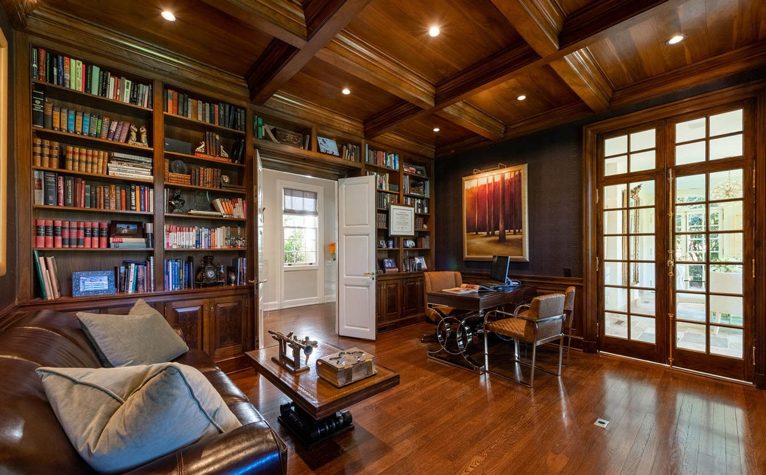 Home office with all wood walls and coffered ceiling with built in shelves and hardwood floors. Matching stain.