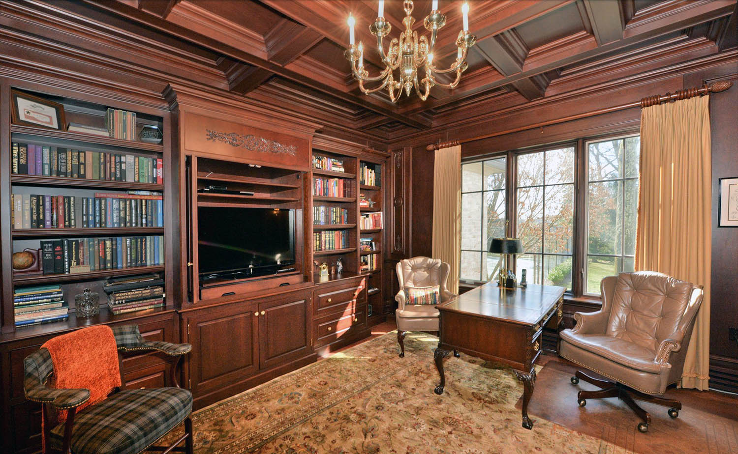 Home office with medium brown stained all wood walls, coffered ceiling and built ins. Hardwood floors.