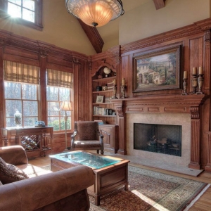 Sitting room with stained wood wall paneling. Vaulted ceiling with wood beams. Fireplace with wood surround. Built in cabinets and shelving.