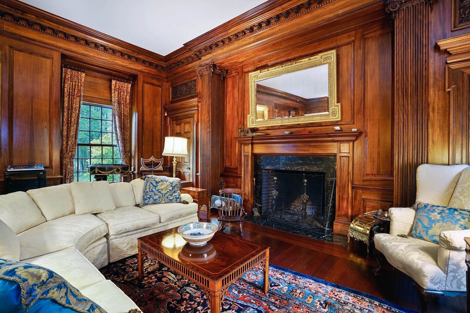 Wooden wall paneling with fireplace. Wood surround. Wood floors. Thick crown molding and custom trim. Plush white sofas.